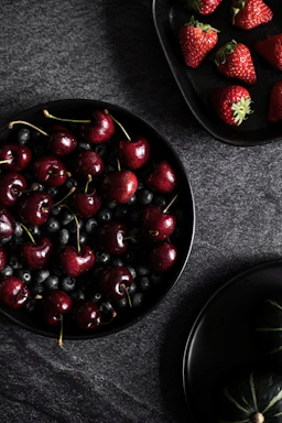 A sleek, dark-toned photo of fresh frozen fruits and vegetables arranged elegantly on a black surface with soft gold accents.