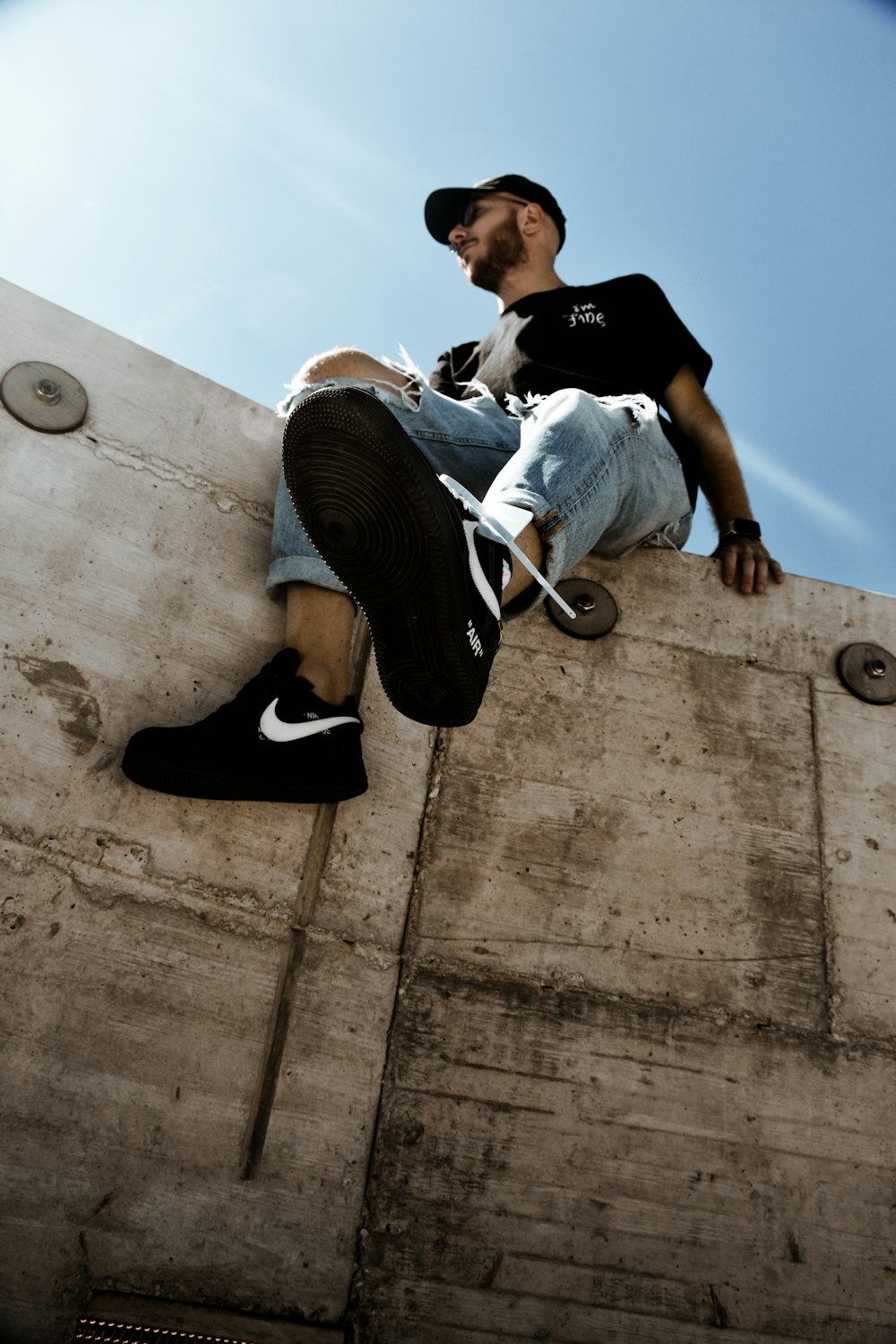man in white shirt and black pants sitting on concrete wall during daytime