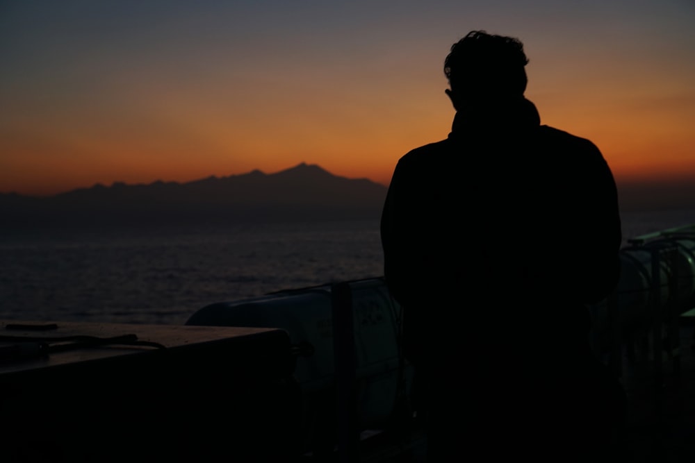 Silueta del hombre de pie cerca del cuerpo de agua durante la puesta del sol