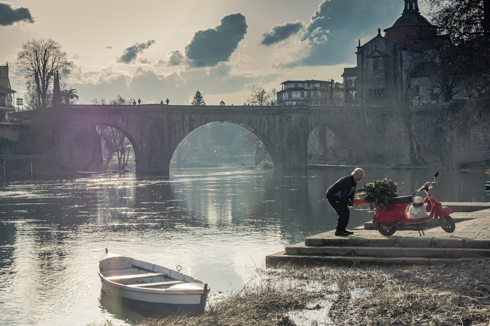 man in black jacket and pants sitting on concrete bench near river during daytime