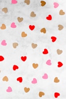 A pattern of various heart shapes scattered across a light gray textured background. The hearts are in shades of red, pink, gold glitter, and brown, creating a playful and decorative arrangement.