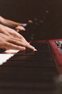 Hands playing a keyboard with sheet music in the background, emphasizing learning.