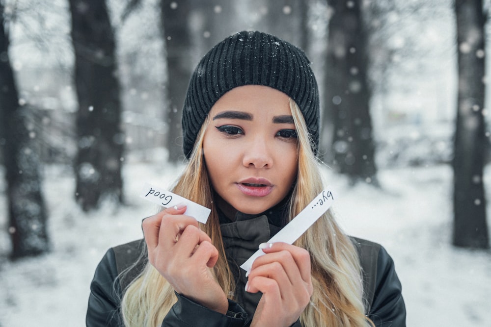 woman in black knit cap and gray jacket holding white printer paper