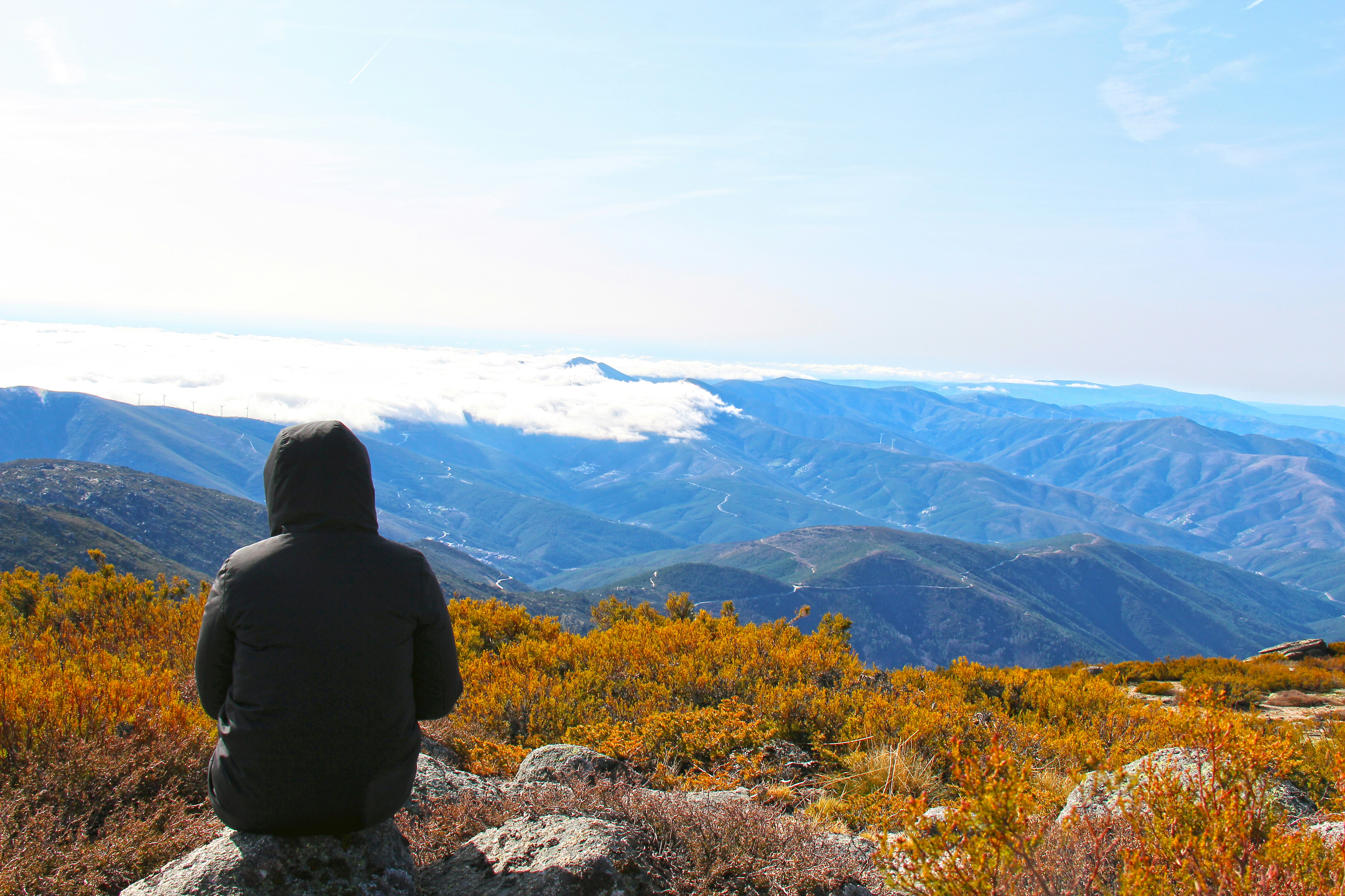 person in black jacket sitting on rock near mountains during daytime, 