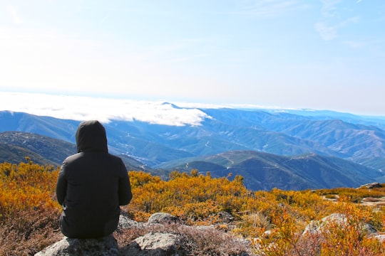 person in black jacket sitting on rock near mountains during daytime in Serra da Estrela Portugal