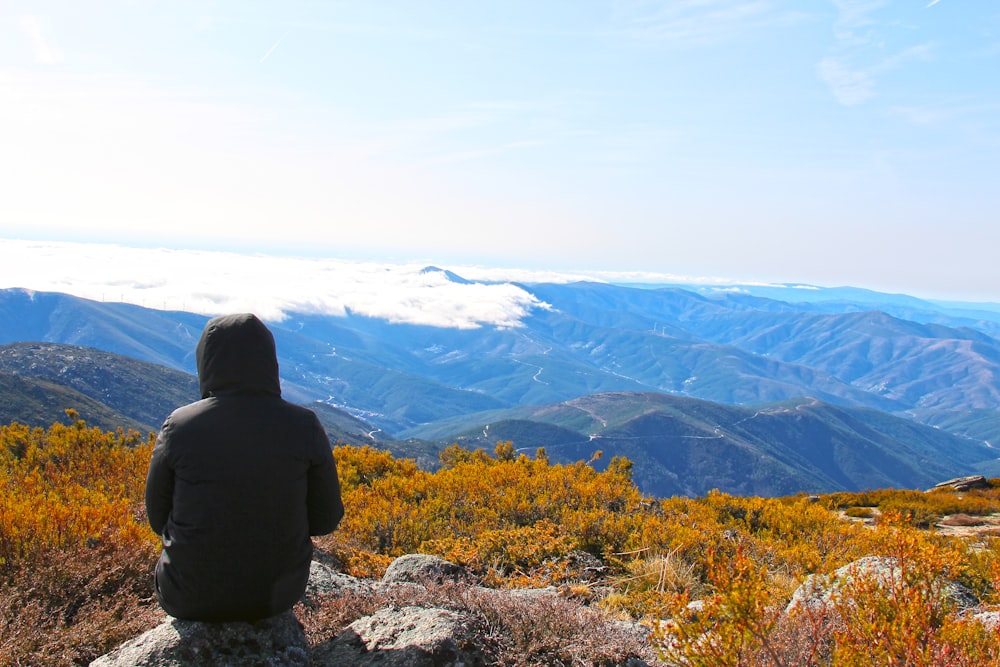 person in black jacket sitting on rock near mountains during daytime