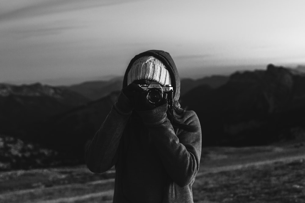 grayscale photo of woman in black jacket holding camera