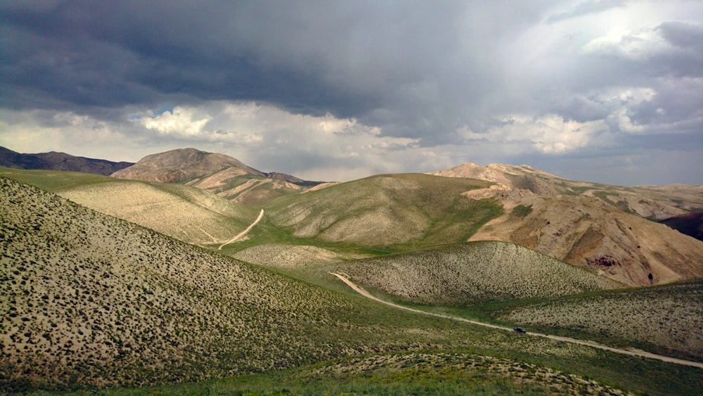 green grass field and mountains under white clouds