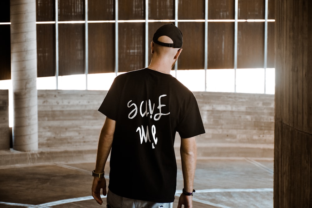 man in black crew neck t-shirt and black cap standing on brown wooden floor