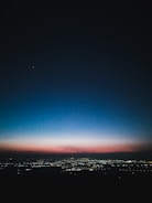 A panoramic cityscape at dusk with deep charcoal skies and glowing emerald accents.