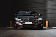 A sleek, dark-colored BMW car is parked against a modern, industrial-looking backdrop. The lighting highlights the glossy surface of the vehicle, emphasizing its design features.