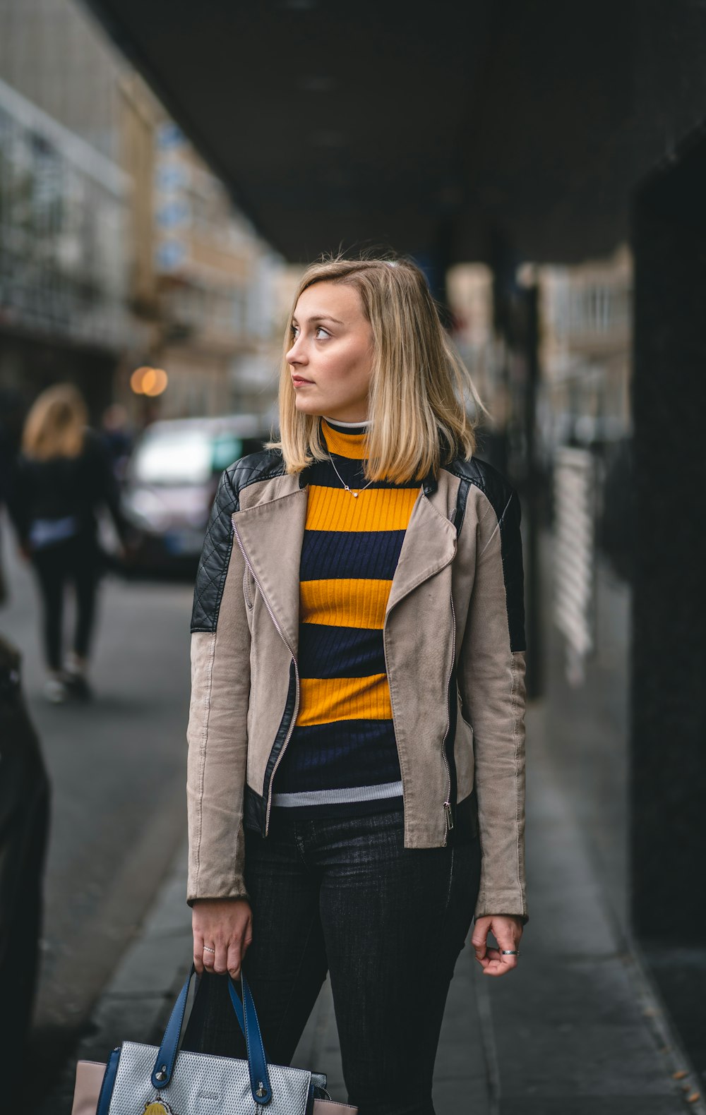 woman in black shirt and brown coat standing on sidewalk during daytime