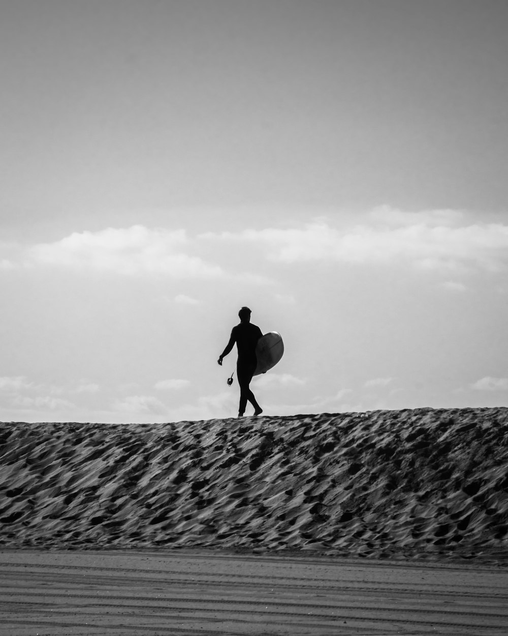 grayscale photo of man walking on sand