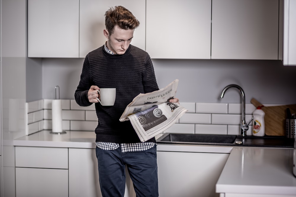 man in black sweater holding white ceramic mug