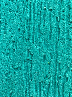A close-up view of a textured surface with a vibrant turquoise color. The surface appears to have granular, uneven patterns resembling small pebbles or grains, creating a visually interesting effect.
