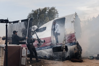 man in black jacket and blue denim jeans standing beside red and white van during daytime