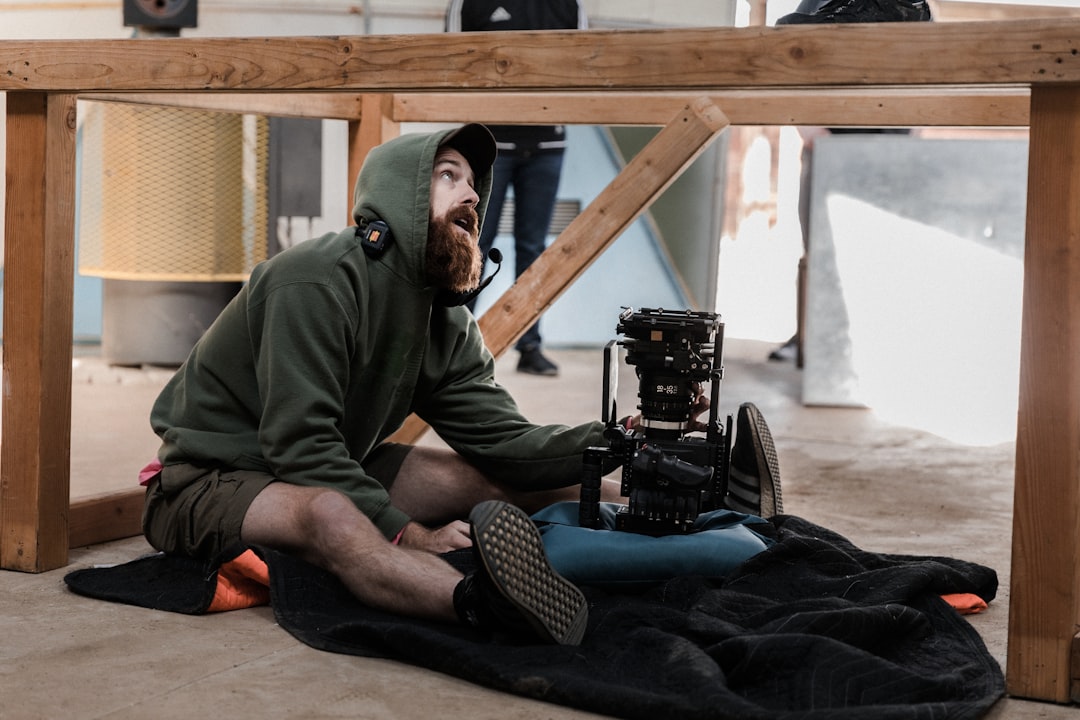 man in green long sleeve shirt and blue denim jeans sitting on floor with camera on on on on on