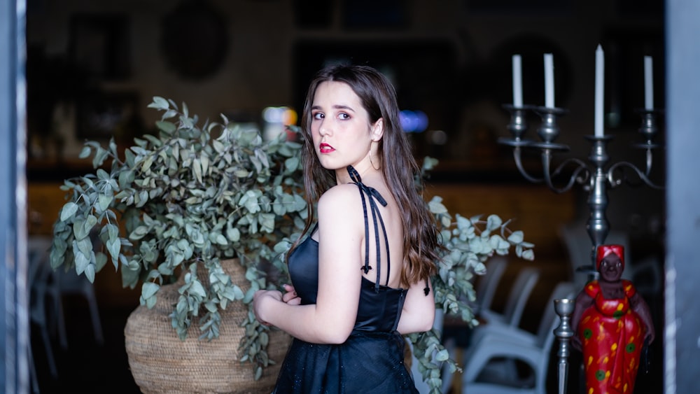 a woman in a black dress standing next to a potted plant