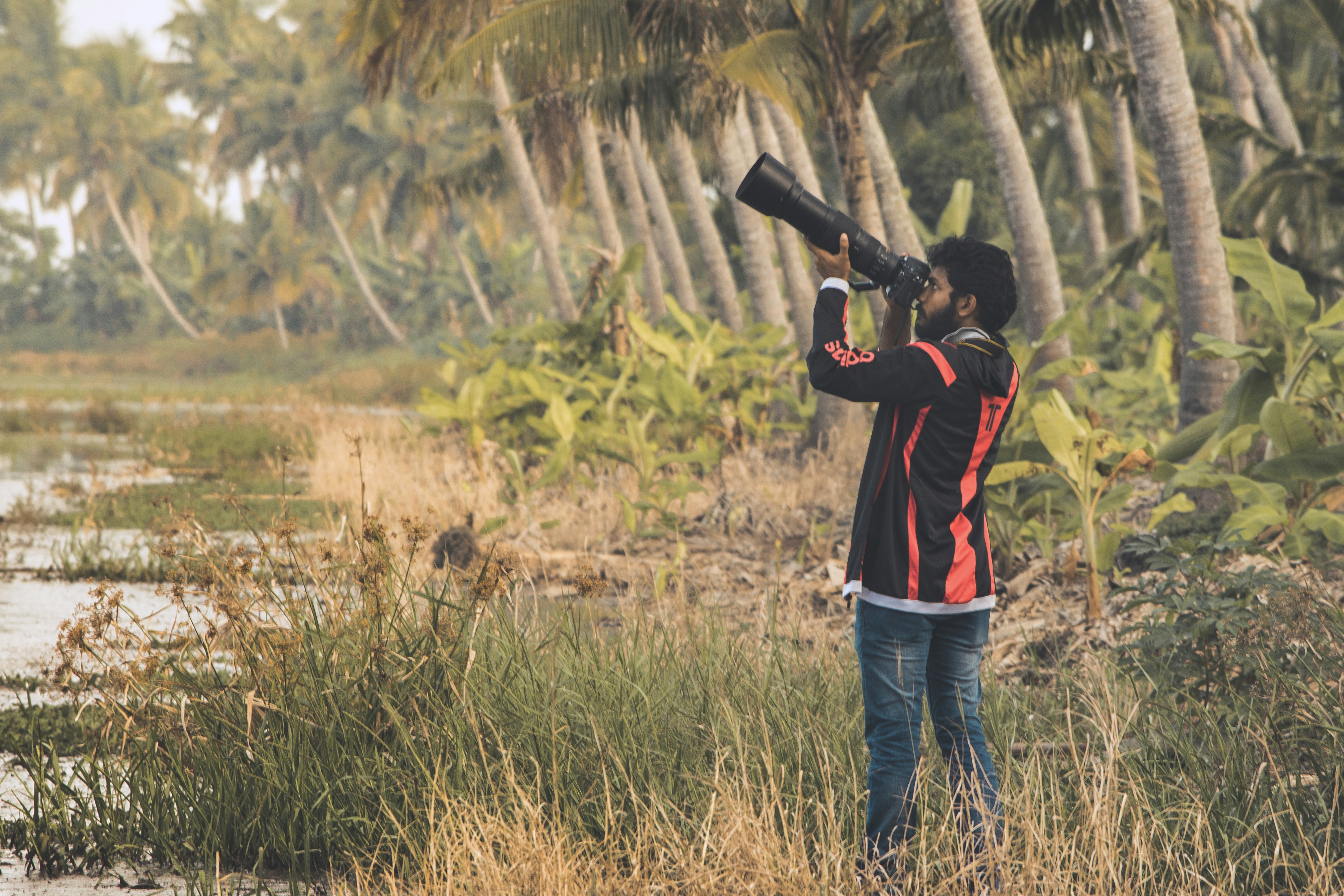 man in black and red jacket holding black dslr camera