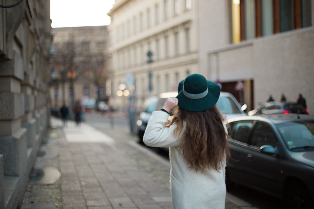 woman in white long sleeve shirt and blue fedora hat standing on sidewalk during daytime