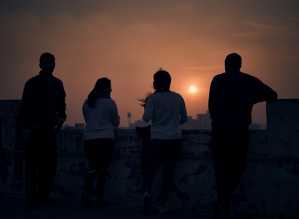 silhouette of people standing on concrete wall during sunset