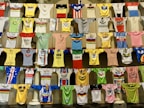 A collection of colorful cycling jerseys is displayed hanging on rows of lines. The jerseys feature various designs, logos, and brands, creating a vibrant and eclectic visual. Each jersey has distinct colors, patterns, and sponsorship logos, highlighting a broad spectrum of cycling history and culture.