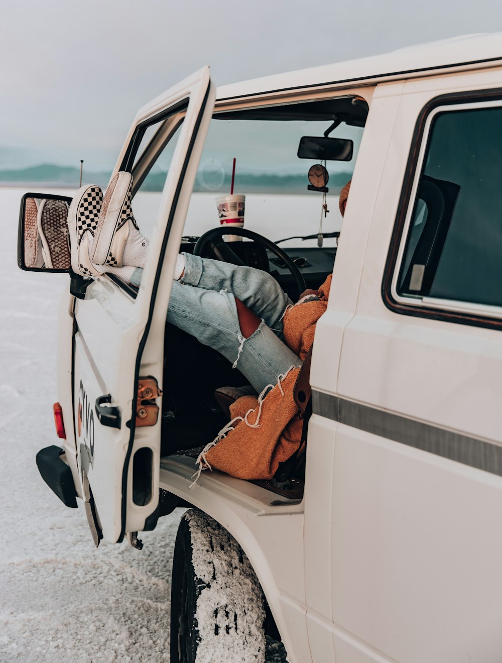 man in white t-shirt and blue denim jeans lying on white van during daytime