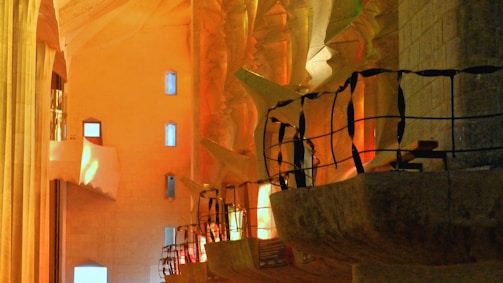 Intricate interior architecture with sculptural columns and railings, illuminated by a warm, ambient light that creates a play of shadows. The design features angular and organic shapes with a combination of smooth and textured surfaces.