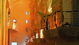 Intricate interior architecture with sculptural columns and railings, illuminated by a warm, ambient light that creates a play of shadows. The design features angular and organic shapes with a combination of smooth and textured surfaces.