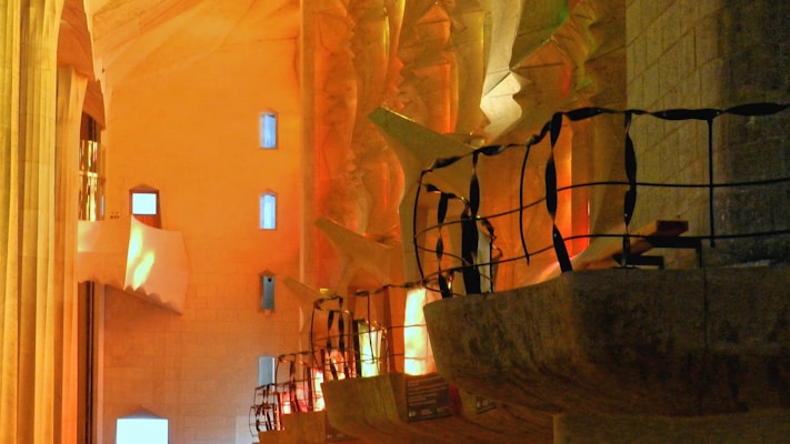 Intricate interior architecture with sculptural columns and railings, illuminated by a warm, ambient light that creates a play of shadows. The design features angular and organic shapes with a combination of smooth and textured surfaces.