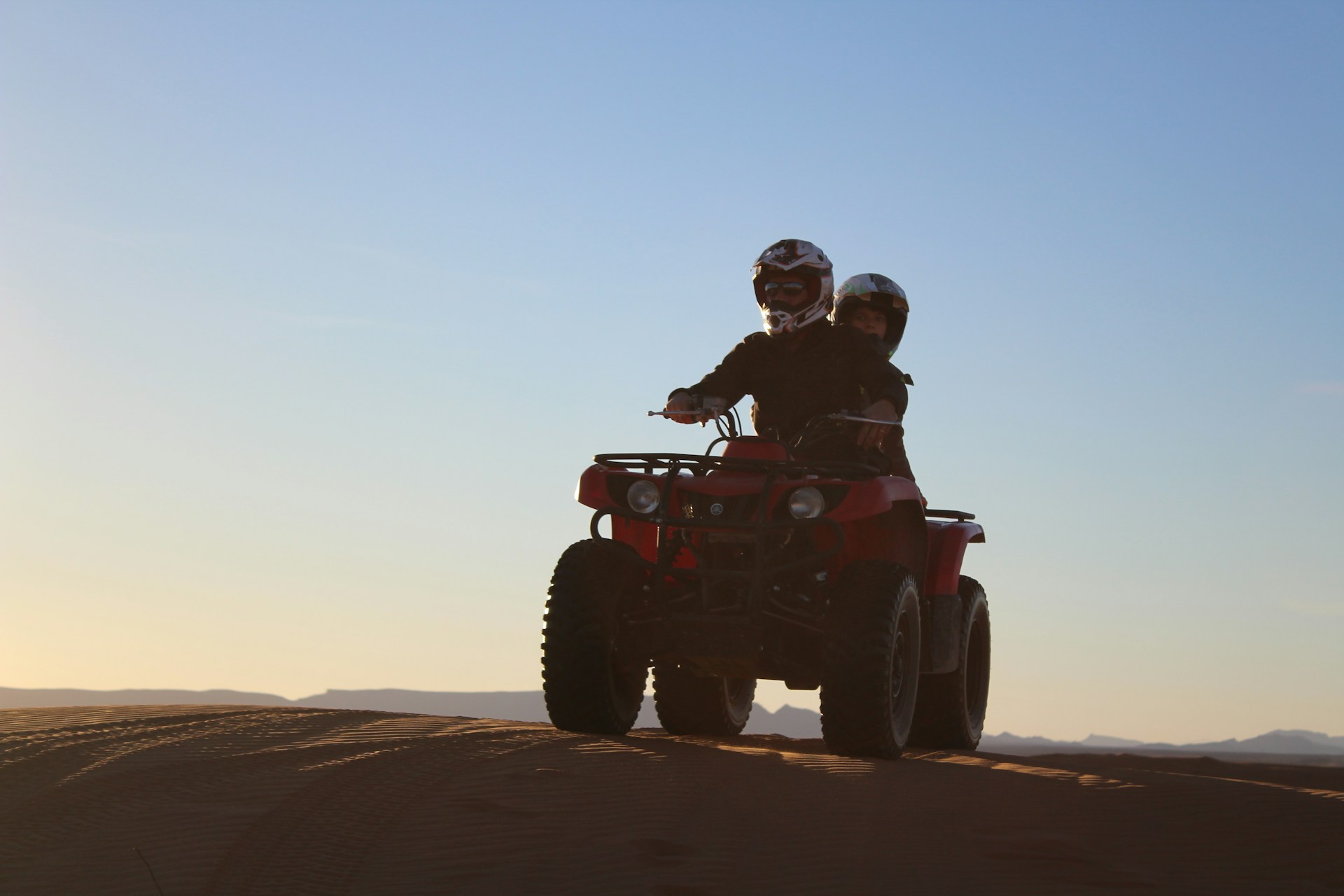 man riding red atv on brown sand during daytime