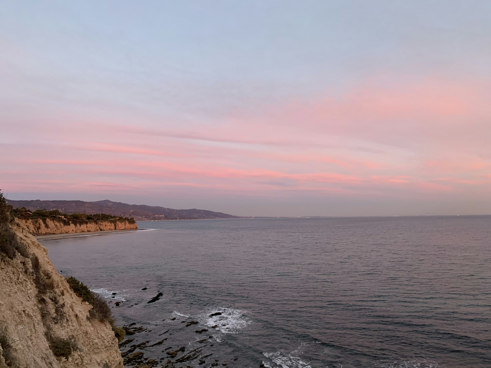A serene dawn view of Isla Isabel’s rocky coastline with gentle waves under a sky painted in soft pink and orange hues.