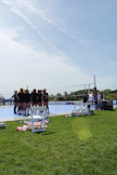 A group of boys and girls in teal and charcoal jerseys practicing volleyball drills on an outdoor court under a bright sky.