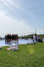 A volleyball coach talking with players during a sunny outdoor training session.