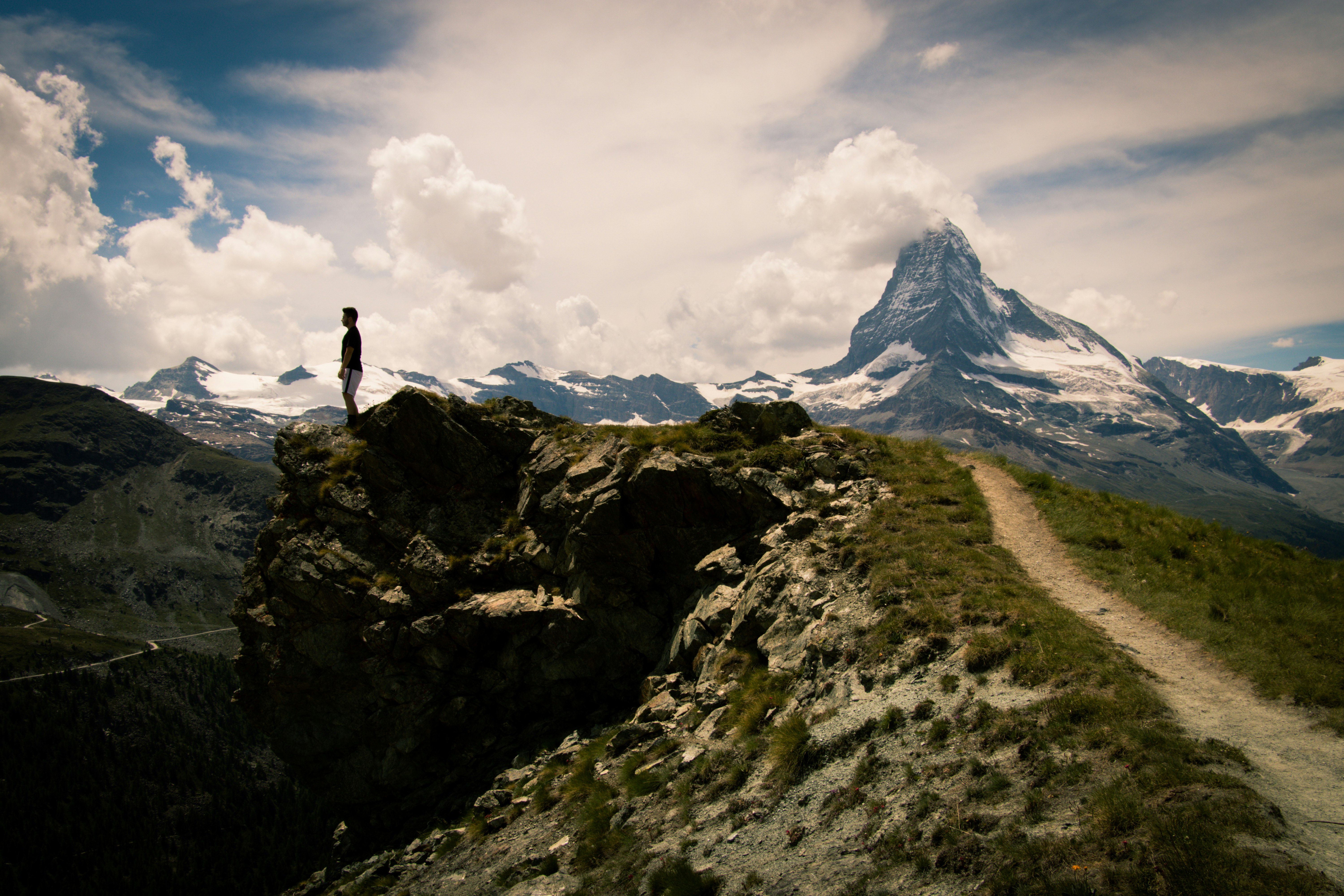 person standing on rock mountain under white clouds during daytime