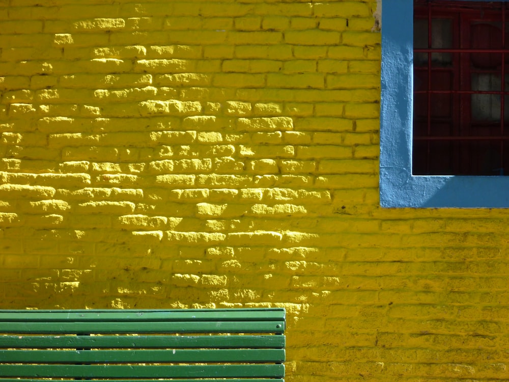 blue wooden bench beside yellow concrete wall