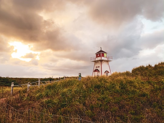 white and red lighthouse on green grass field under cloudy sky during daytime in Prince Edward Island National Park Canada