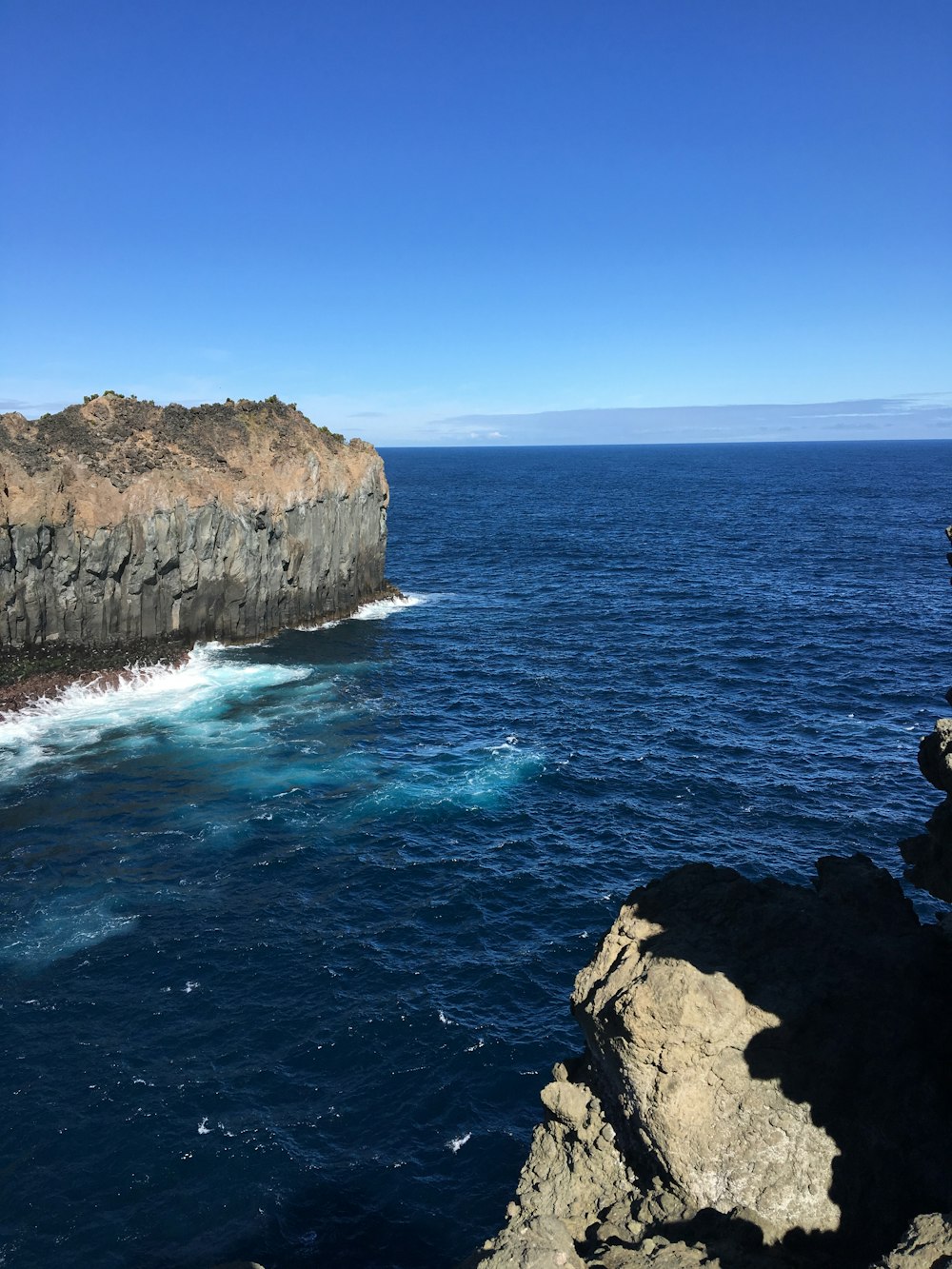 brown rocky mountain beside blue sea under blue sky during daytime