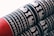 The image features a fabric with intricate patterns in white woven onto a black background. The patterns include geometric shapes and representations of animals or objects, repeated in horizontal rows. The lower portion of the fabric is a solid red color, providing contrast to the patterned section.