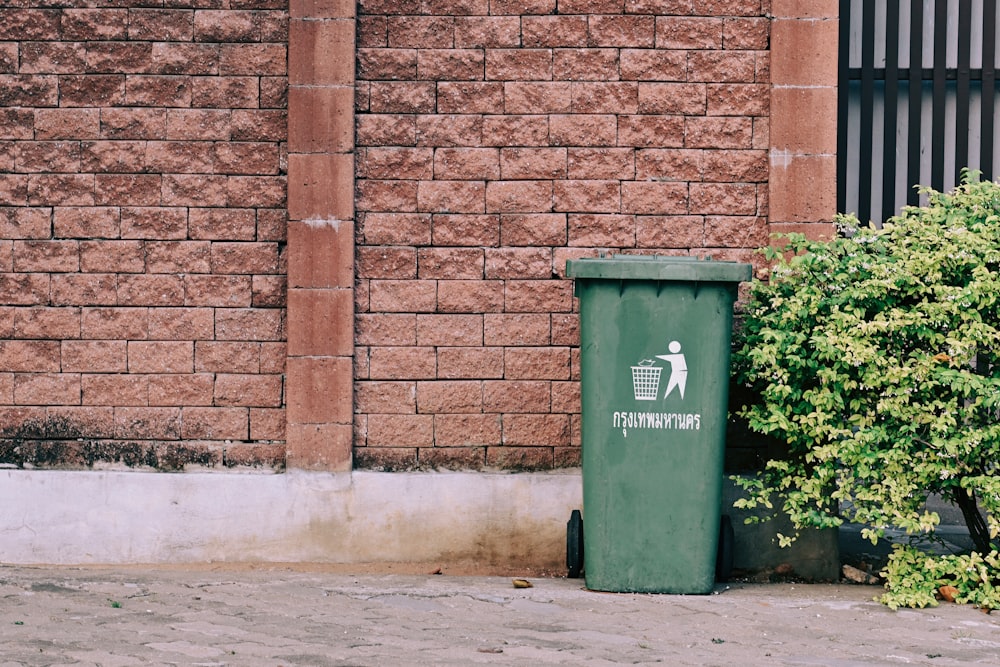 green trash bin beside brown brick wall