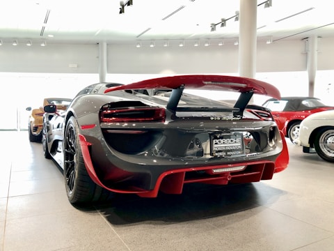 A sleek, high-performance sports car is prominently displayed indoors, highlighting its glossy finish and aerodynamic design. Surrounding it are other luxurious cars, suggesting a showroom setting.