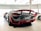 A sleek, high-performance sports car is prominently displayed indoors, highlighting its glossy finish and aerodynamic design. Surrounding it are other luxurious cars, suggesting a showroom setting.