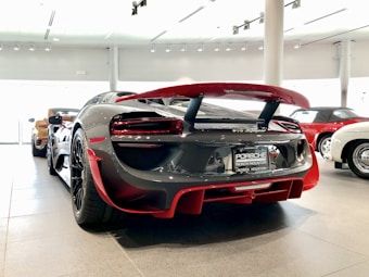 A sleek, high-performance sports car is prominently displayed indoors, highlighting its glossy finish and aerodynamic design. Surrounding it are other luxurious cars, suggesting a showroom setting.