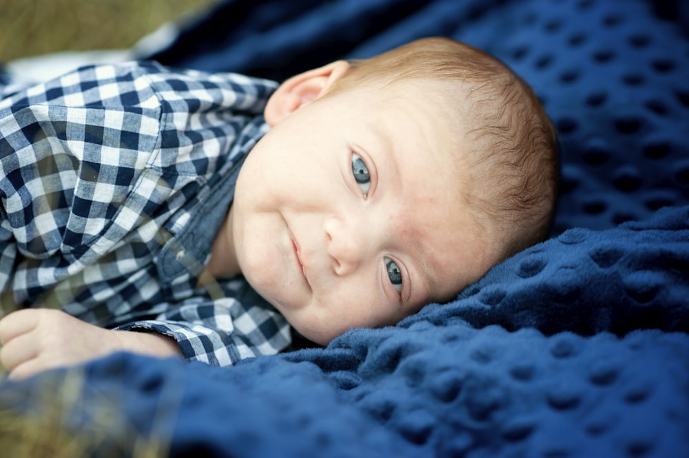 boy in blue white and black plaid shirt lying on blue textile