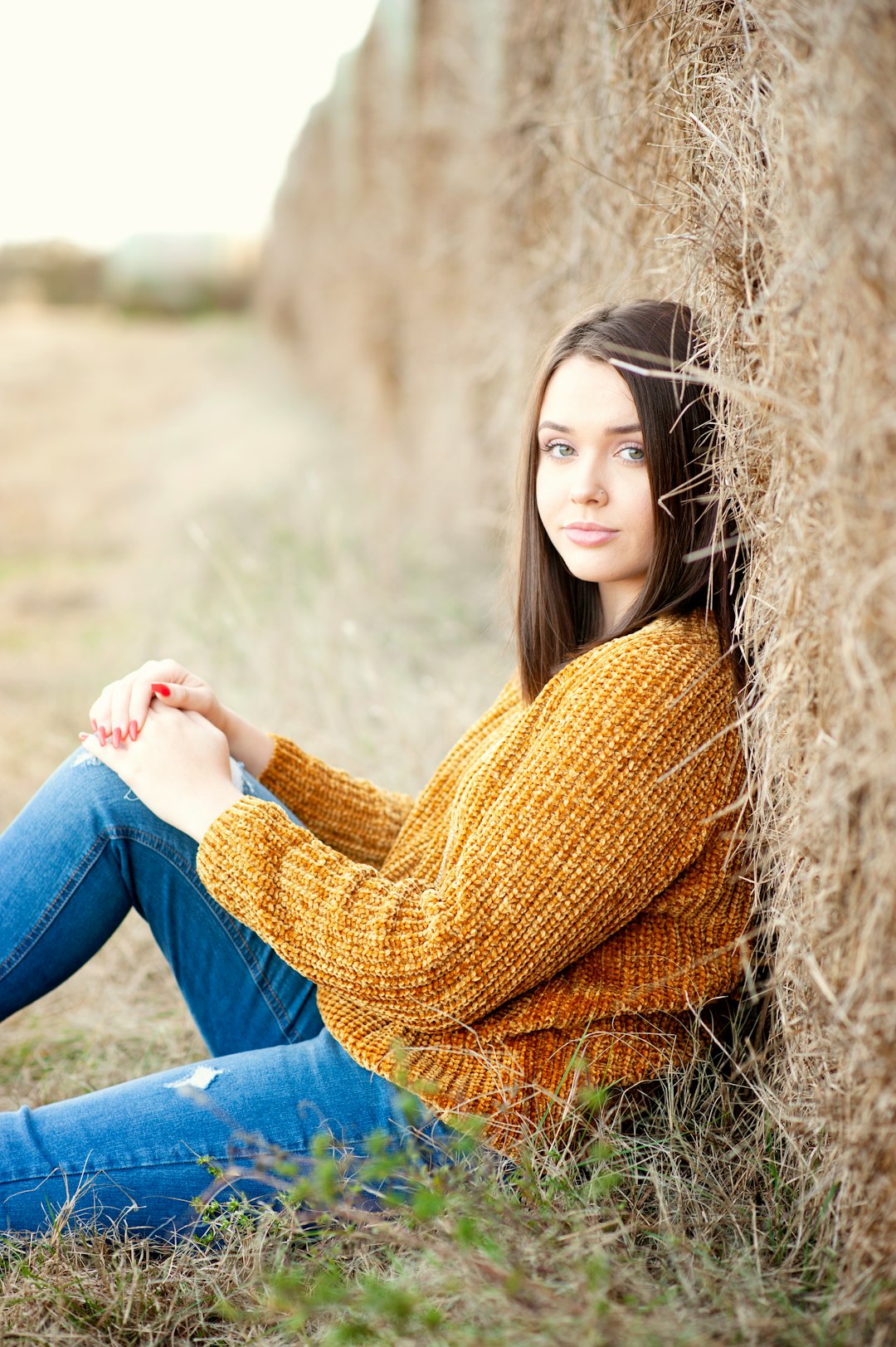 woman in yellow knit sweater and blue denim jeans sitting on brown grass field during daytime