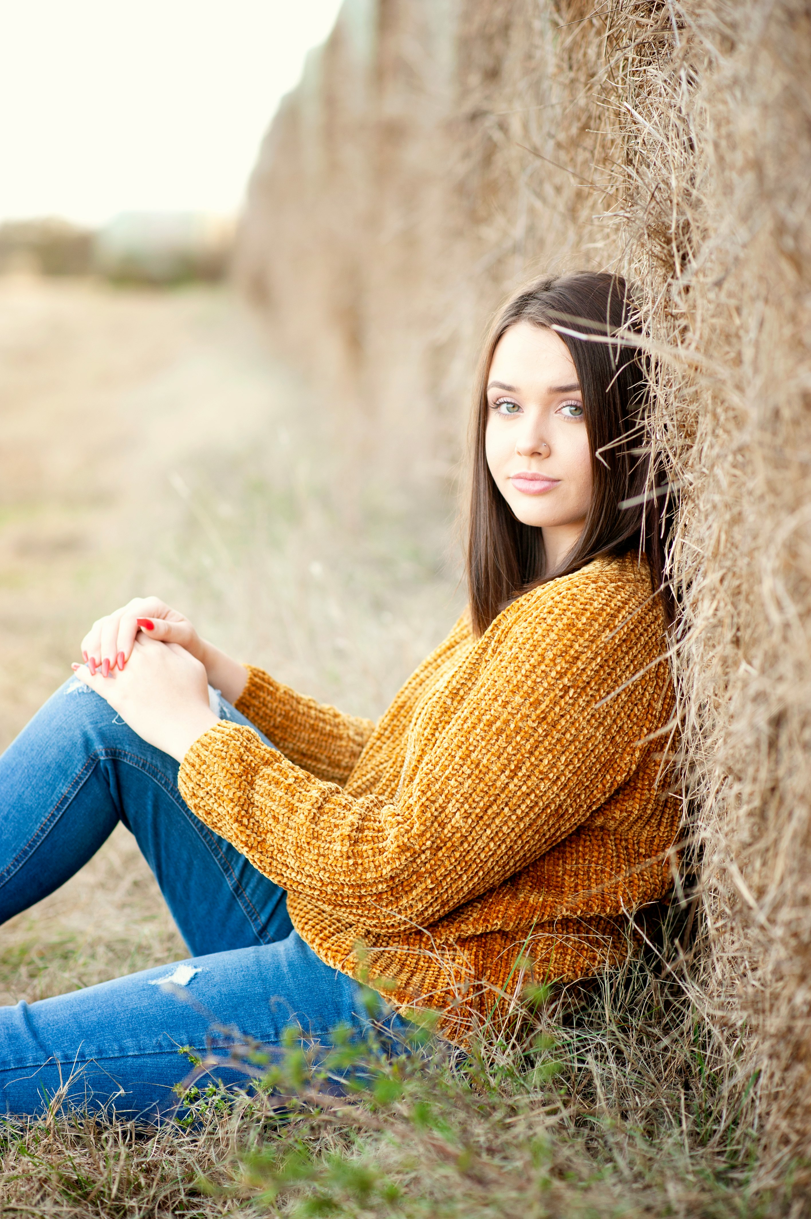 woman in yellow knit sweater and blue denim jeans sitting on brown grass field during daytime