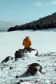 person in yellow jacket sitting on snow covered ground during daytime