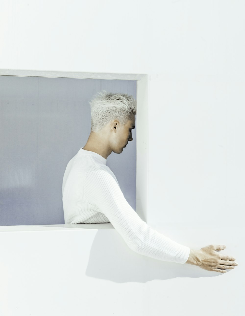 man in white sweater leaning on white wall