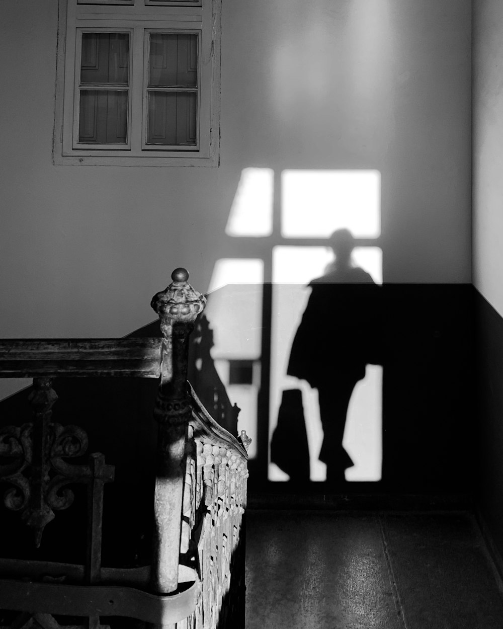 grayscale photo of woman in dress standing near window