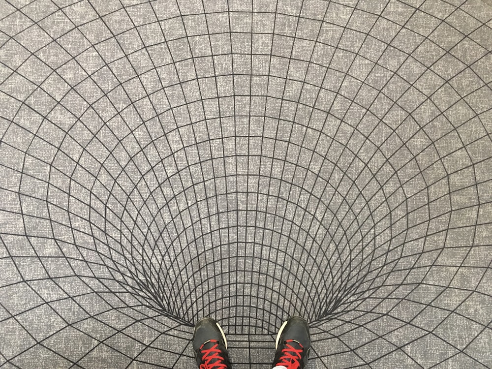 person in black and red sneakers standing on white and black ceramic tiles